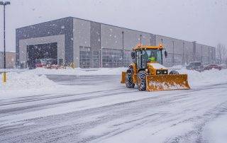 Plow truck and skid steer clearing snow in a large Colorado Springs commercial parking lot